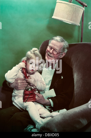 Negli anni quaranta anni cinquanta nipote seduta sul sorridente nonno giro parlando al telefono giocattolo Foto Stock
