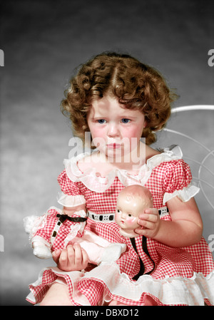 Negli anni quaranta anni cinquanta ragazza indossando rosso Gingham controllato abito a piangere tenendo rotto la testa delle bambole Foto Stock