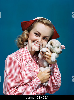 Negli anni quaranta anni cinquanta ritratto bionda sorridente ragazza TEEN INDOSSA Red & White controllato camicetta & stile olandese HAT HOLDING SPITZ cucciolo a guancia Foto Stock