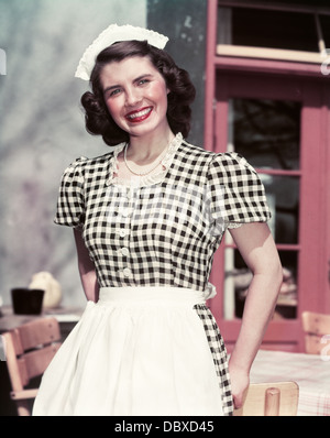 Negli anni quaranta anni cinquanta sorridente donna vestita di nero e bianco a scacchi cameriera vestito Abito in pizzo CATENARIA CAP guardando la fotocamera Foto Stock