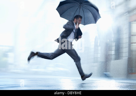 Imprenditore in esecuzione con ombrello in rainy street Foto Stock