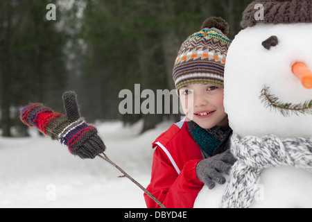 Chiusura del ragazzo sorridente dietro il pupazzo di neve Foto Stock