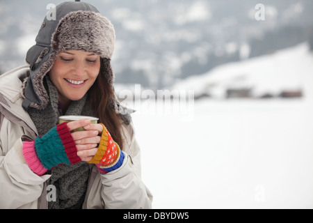Donna sorridente di bere il caffè nella neve Foto Stock