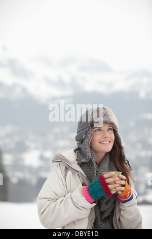 Donna sorridente di bere il caffè in campo nevoso Foto Stock