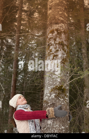 Donna sorridente che abbraccia tronco di albero nei boschi Foto Stock