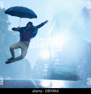 Entusiastico Uomo con ombrello jumping in Rain Foto Stock