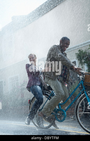 Coppia felice equitazione Bicicletta in rainy street Foto Stock