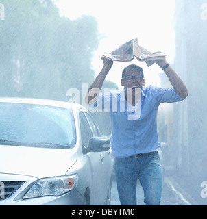 Uomo sorridente azienda giornale overhead in rainy street Foto Stock