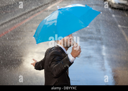 Imprenditore con piccolo ombrello a piedi sotto la pioggia Foto Stock