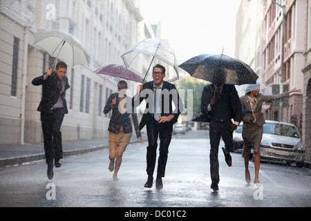 La gente di affari con ombrelloni in esecuzione in rainy street Foto Stock