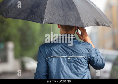 L'uomo parlando al cellulare sotto ombrello in caso di pioggia Foto Stock