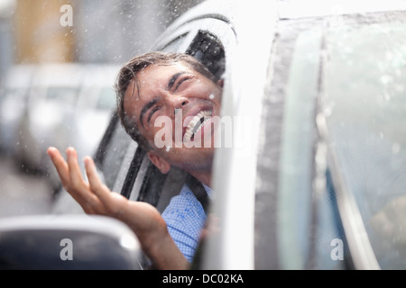 Entusiastico uomo in macchina a guardare fuori dalla finestra a pioggia Foto Stock