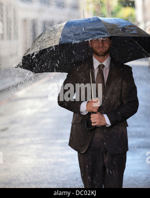 Happy businessman con ombrellone a piedi nella rainy street Foto Stock