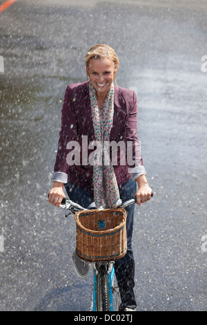 Donna felice equitazione Bicicletta in rainy street Foto Stock