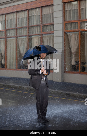 Imprenditore in piedi sotto ombrellone rotto in rainy street Foto Stock