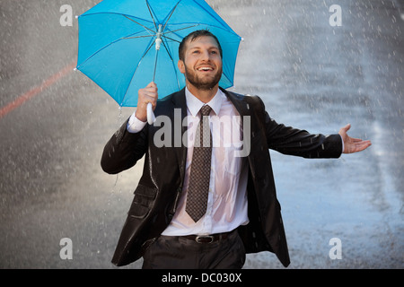 Imprenditore entusiasta con piccolo ombrello in rainy street Foto Stock