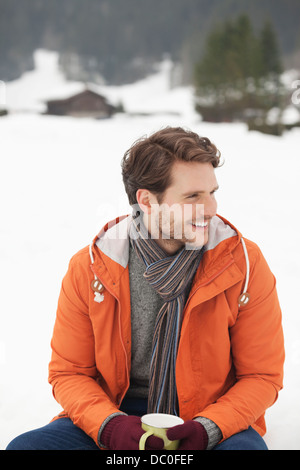 Uomo sorridente di bere il caffè in campo nevoso Foto Stock