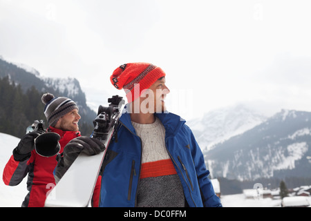 Sorridendo gli uomini che trasportano gli sci ai piedi della montagna Foto Stock