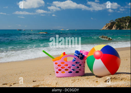 Rosa borsa da spiaggia e sfera colorata nella sabbia vicino alla linea di acqua presso la spiaggia di spagnolo Foto Stock