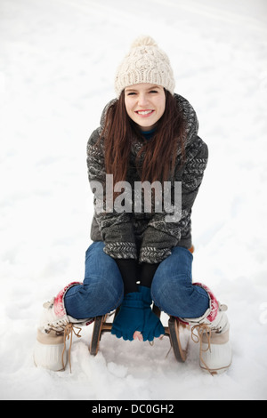 Ritratto di donna sorridente seduto sulla slitta nella neve Foto Stock
