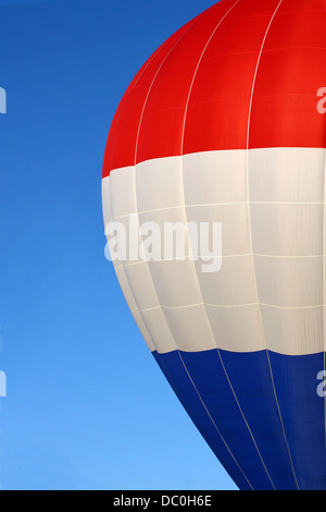 Una stretta fino a metà del lato di un rosso, bianco e blu della mongolfiera, volare nella parte anteriore di un luminoso Cielo di estate blu sullo sfondo Foto Stock