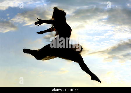 Una giovane donna attraente è un salto in aria di fronte a un bel cielo sunsetting Foto Stock