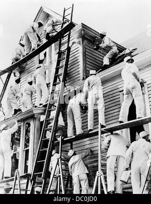 1930 Gruppo 18 uomini pittori IN BIANCO tute da lavoro tute su scale e ponteggi verniciatura di un parquet massiccio telaio in legno HOUSE Foto Stock