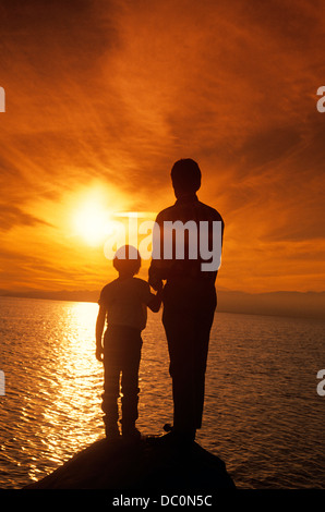 Anni Novanta stagliano padre e figlio guardando il tramonto sull'acqua Foto Stock