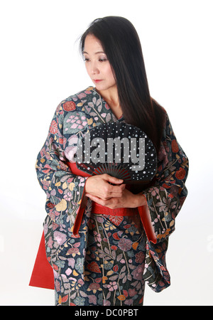 Giapponese signora seduta sul pavimento indossando un tradizionale di blu e di rosso modellato kimono e tenendo una ventola Foto Stock
