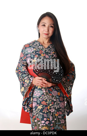Giapponese signora seduta sul pavimento indossando un tradizionale di blu e di rosso modellato kimono e tenendo una ventola Foto Stock