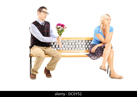 Voce maschile dando un mazzo di fiori e disinteressato femmina bionda seduta su una panca in legno Foto Stock