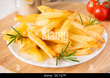 Porzione di le patate fritte fatte in casa (patate) con rosmarino sulla piastra bianca e tagliere di legno, orizzontale, close up Foto Stock