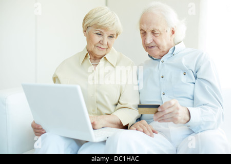 Coppia senior con carta di credito e il computer portatile durante lo shopping tramite Internet Foto Stock