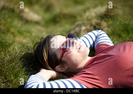 Giovane donna indossa forma di cuore occhiali da sole sdraiati sull'erba Foto Stock