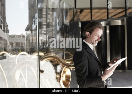 Adulto medio imprenditore appoggiata contro la finestra del negozio e con tavoletta digitale Foto Stock