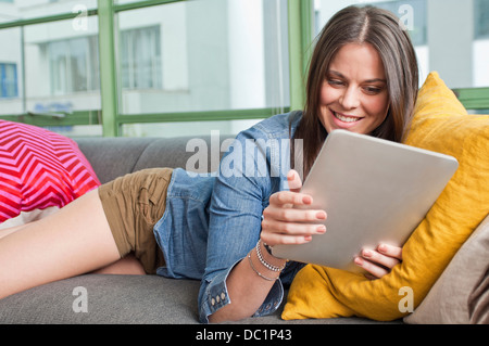 Giovane donna sdraiata sul divano holding tavoletta digitale Foto Stock