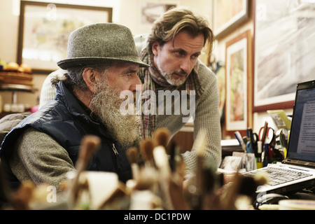 Senior e metà uomo adulto utilizzando laptop in negozio di antiquariato Foto Stock