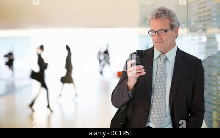 Imprenditore per la messaggistica di testo con un telefono cellulare nella lobby Foto Stock