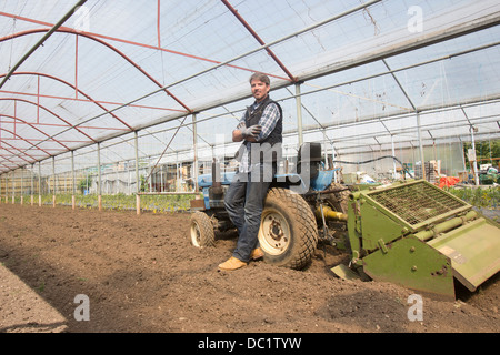 Ritratto di agricoltore biologico con il trattore in polytunnel Foto Stock