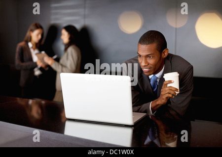 Imprenditore sorridente a bere caffè e utilizzo di computer portatile Foto Stock