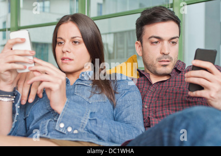 Coppia giovane di casa utilizzando i telefoni cellulari Foto Stock