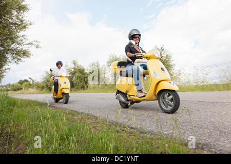 Giovane su scooter riding giù strada rurale Foto Stock