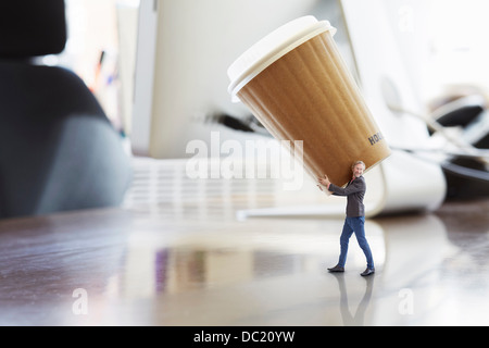 Imprenditore maturo che trasportano grandi tazza monouso sulla scrivania di grandi dimensioni Foto Stock