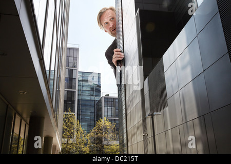 Imprenditore sovradimensionato da peering dietro i grattacieli, basso angolo di visione Foto Stock