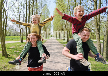 Il padre e la madre racing con due ragazzi sulle spalle attraverso park Foto Stock