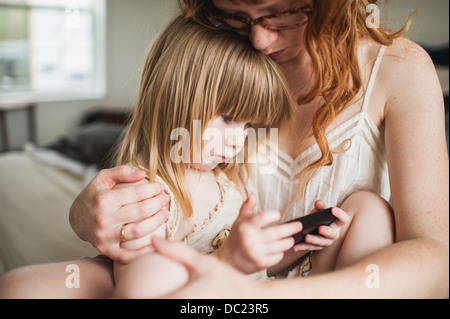 La madre abbraccia la figlia, utilizza lo smartphone Foto Stock