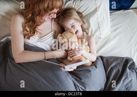 Madre e figlia giacente sul letto cuddling giocattolo morbido Foto Stock