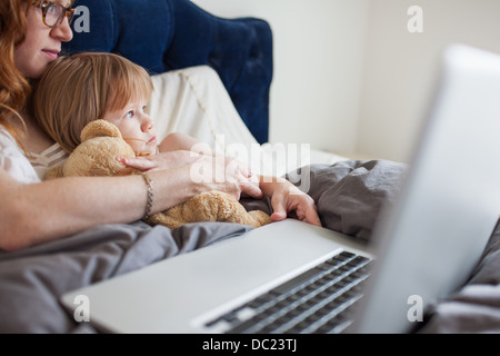 Madre e figlia giacente in letto con il computer portatile Foto Stock