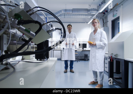 Due scienziati indossando camici da laboratorio e occhiali di sicurezza in piedi in laboratorio Foto Stock