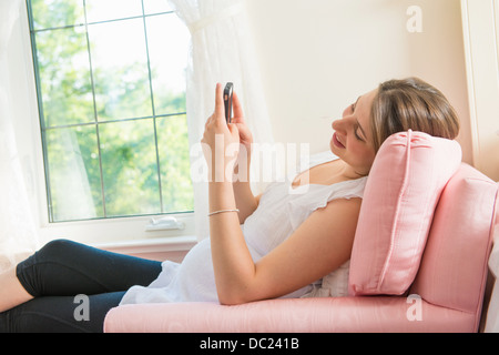 Donna incinta seduta sulla poltrona utilizza lo smartphone Foto Stock